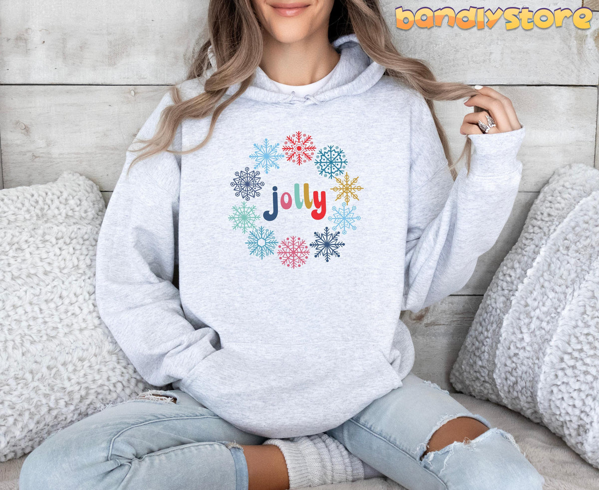 Christmas Snowflake Jolly Hoodie in ash on a seated person against wood planks with fluffy pillows.
