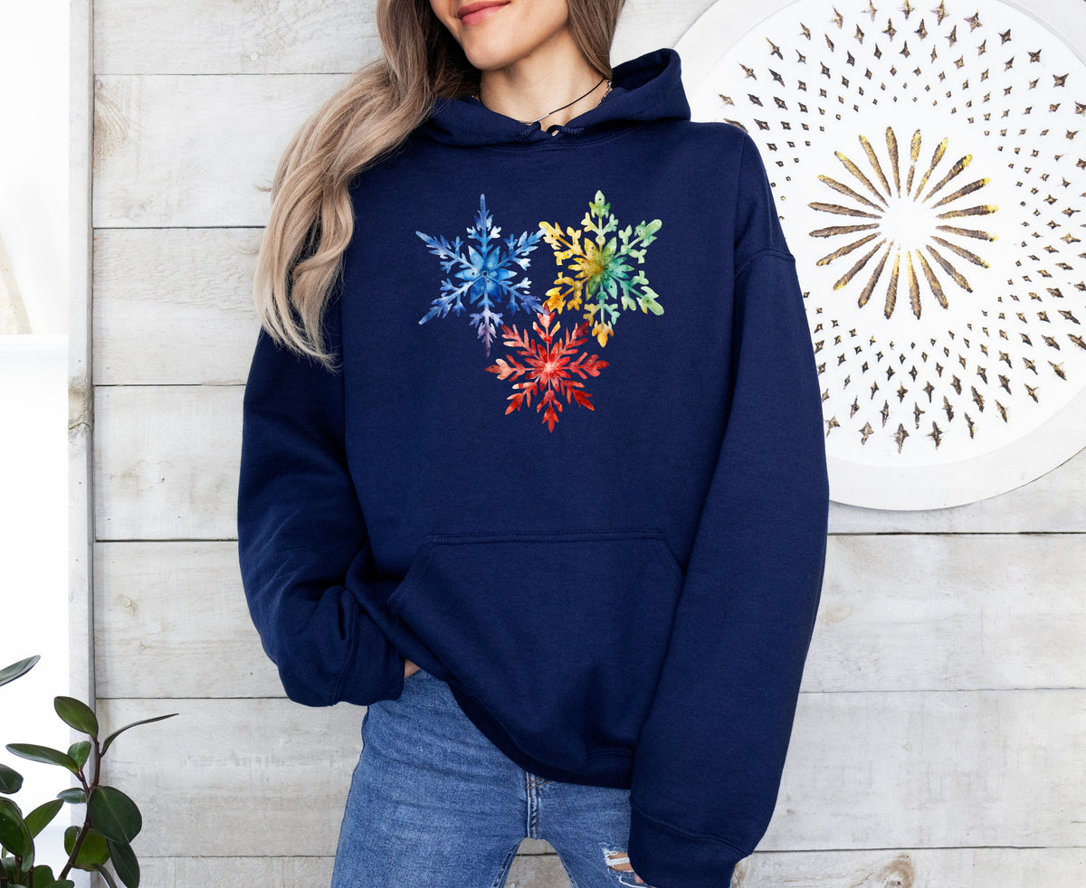 Colorful Watercolor Snowflakes Hoodie in navy, front view on a person against white wood with a gold wall disc and plant.