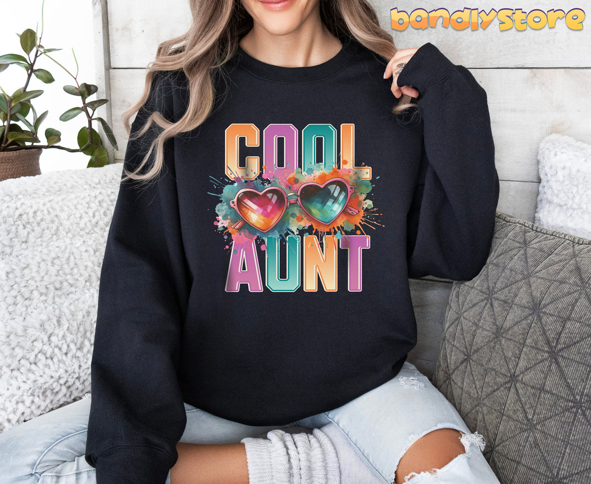 Cool Aunt Sweatshirt in black on a person seated facing forward amid couch pillows and a plant.