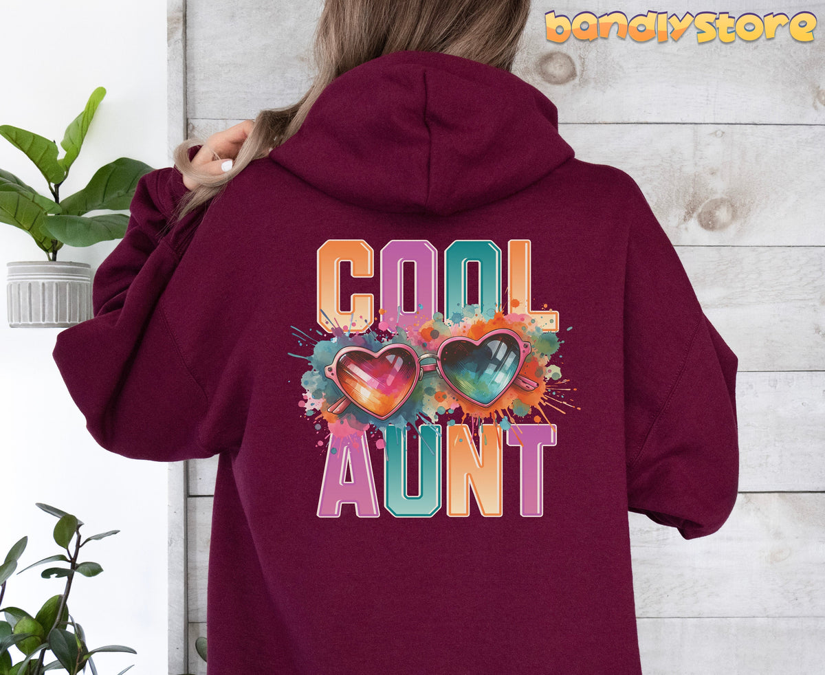 Cool Aunt Hoodie in maroon shown from the back on a person beside a potted plant against a wooden wall.