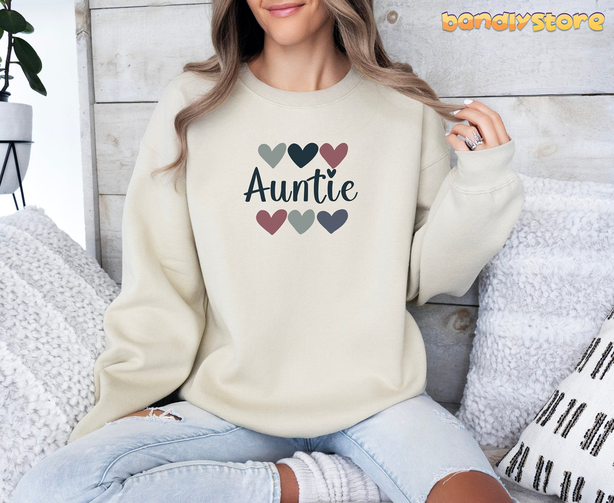 Auntie Sweatshirt in sand on a seated model against light wood with white pillows and a plant.