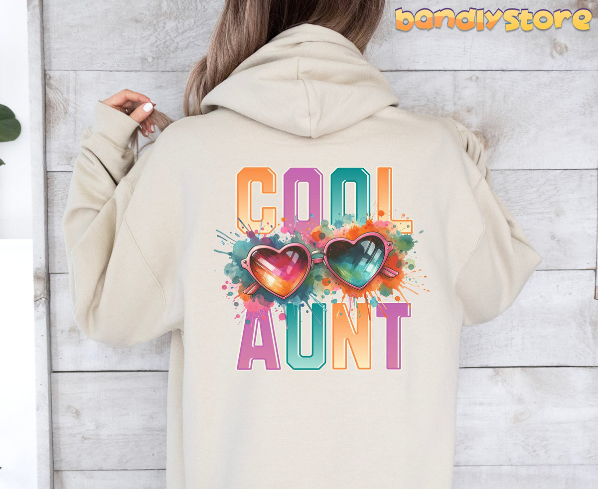 Cool Aunt Hoodie in sand worn from behind against a light wooden wall beside a plant.