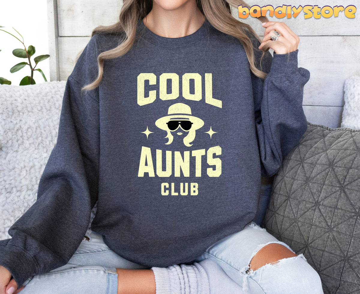 Cool Aunts Club Sweatshirt in dark heather on a seated woman by wood wall with pillows and plant.
