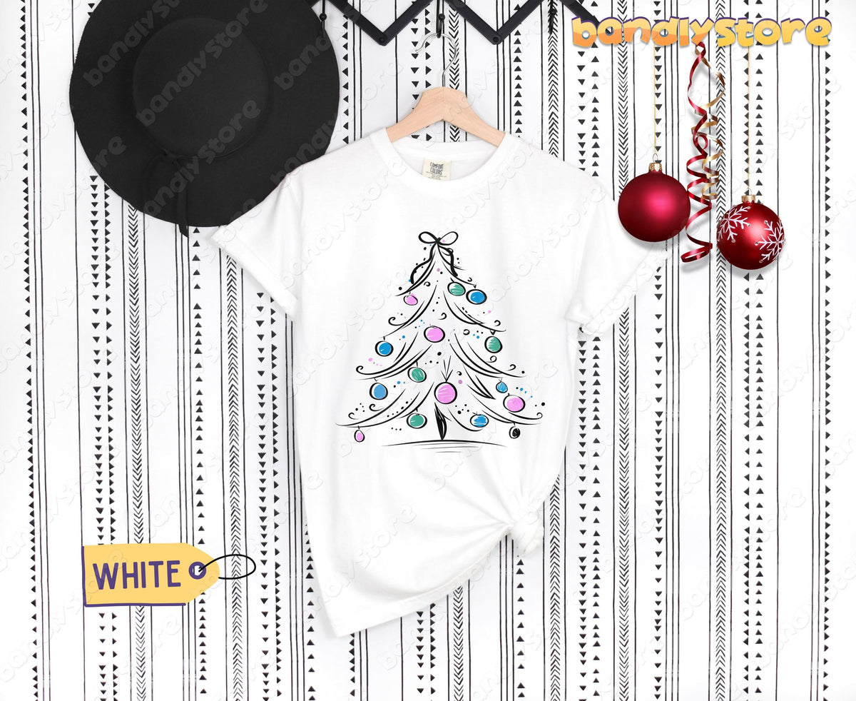 Coquette Christmas Tree T-Shirt white on hanger against patterned wall with black hat and red ornaments.
