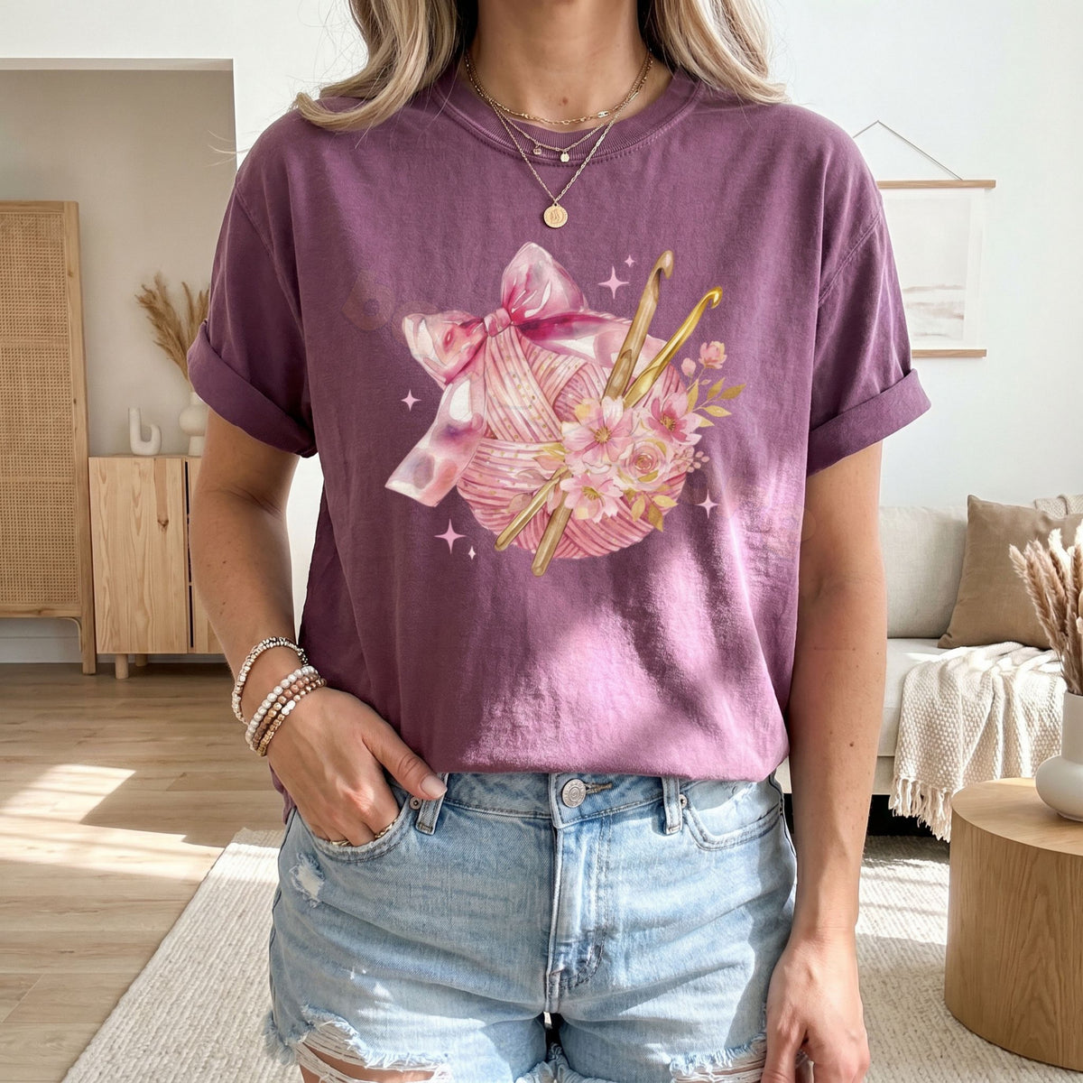 Coquette Crocheting T-Shirt in Berry worn front-facing in a living room with wooden furniture, sofa, and plants.