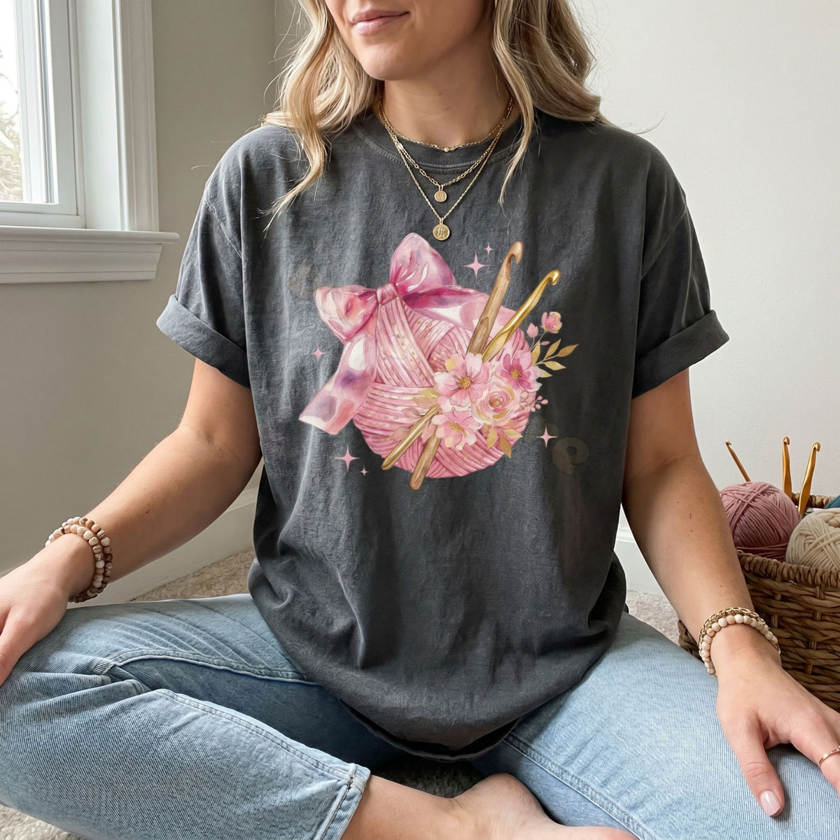 Coquette Crocheting T-Shirt in Pepper, worn by a seated woman with yarn basket nearby.