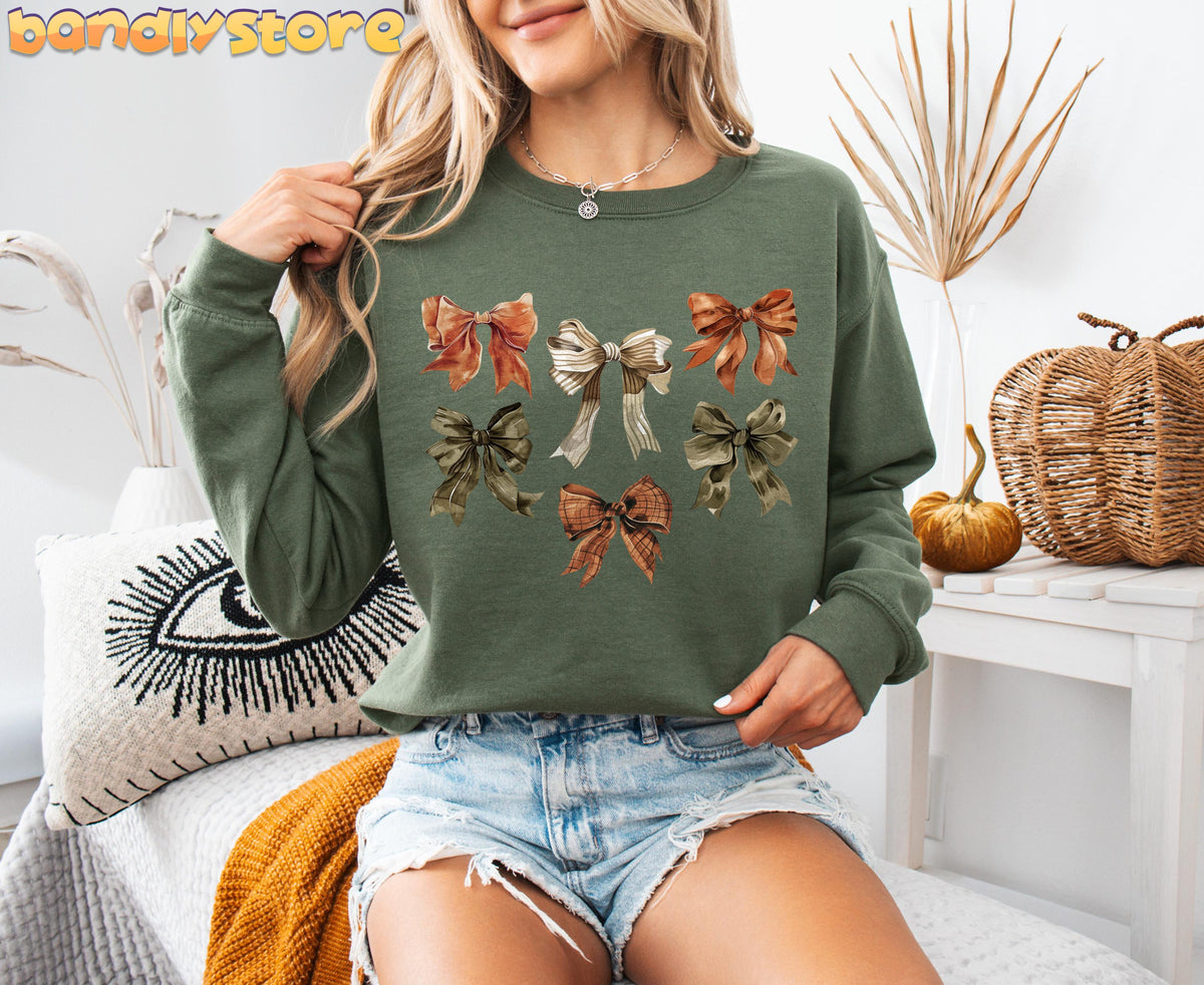 Fall Coquette Bow Sweatshirt in military green on a seated model indoors with pumpkins and dried plants.