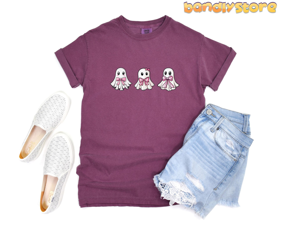Cute Coquette Ghost T-Shirt in berry flat-laid beside white slip-ons and denim shorts.