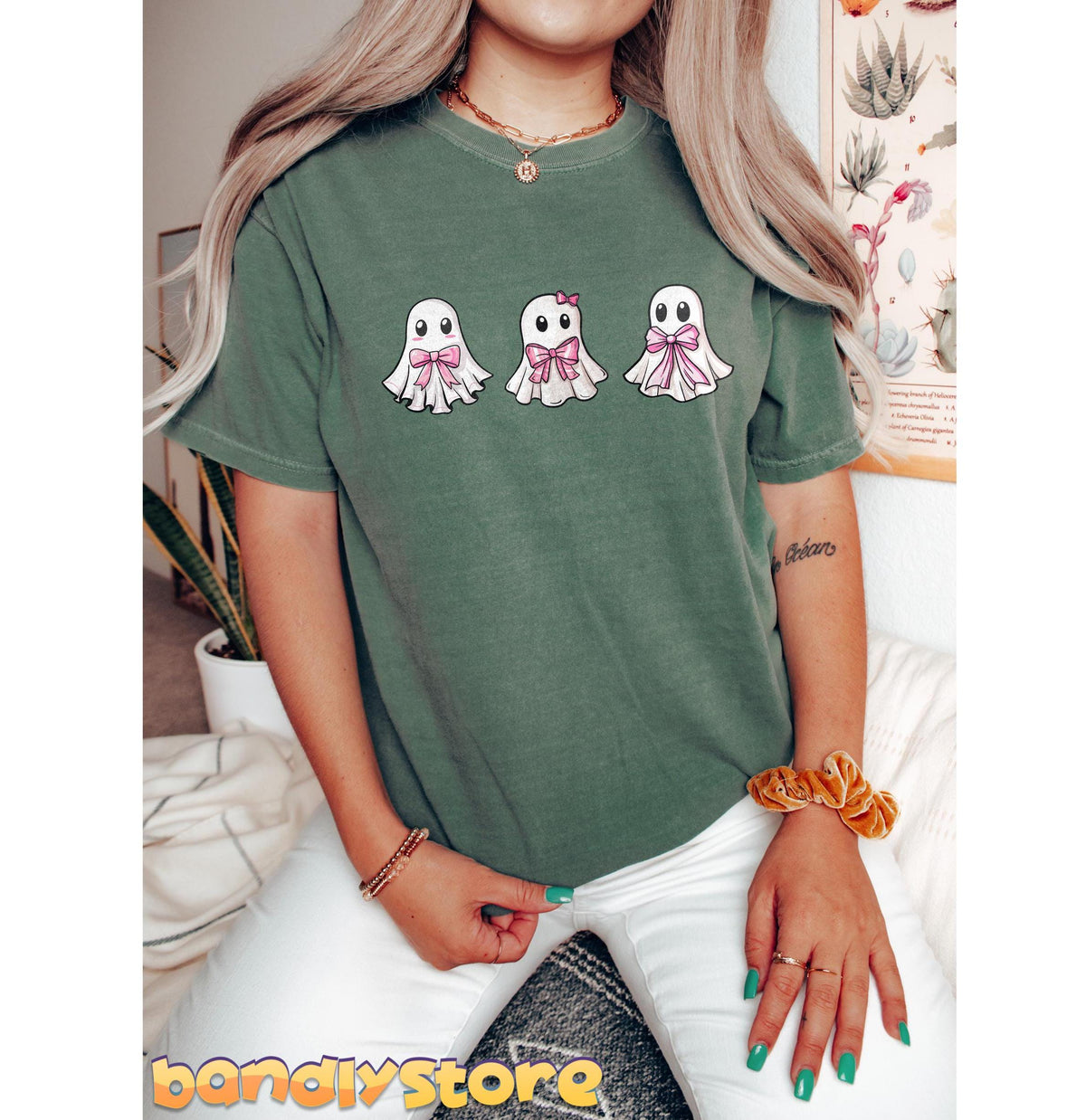 Cute Coquette Ghost T-Shirt in moss, front view on seated wearer beside plant and botanical print.