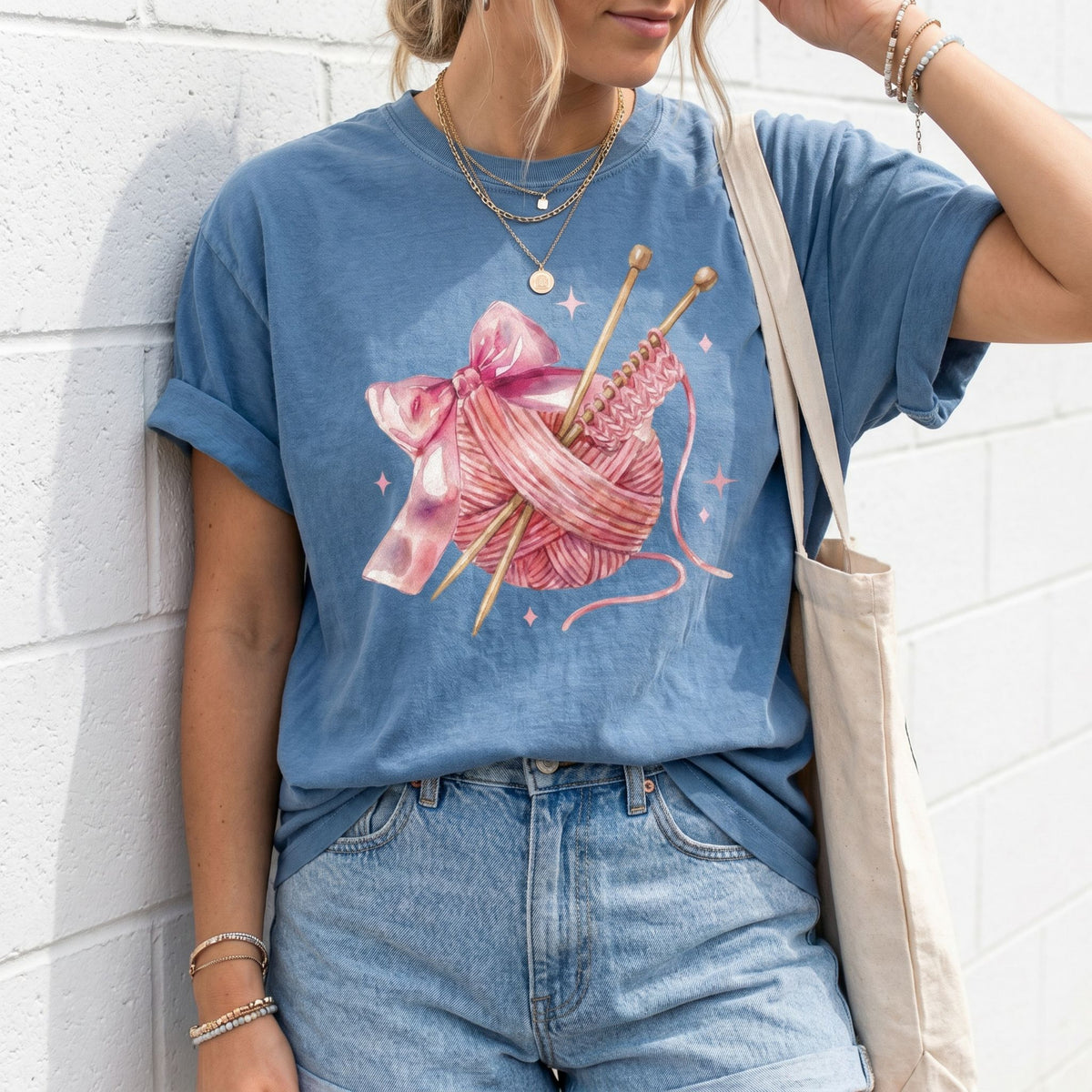 Cute Coquette Knitting T-Shirt in Blue Jean on person against white brick wall with jeans and tote bag.