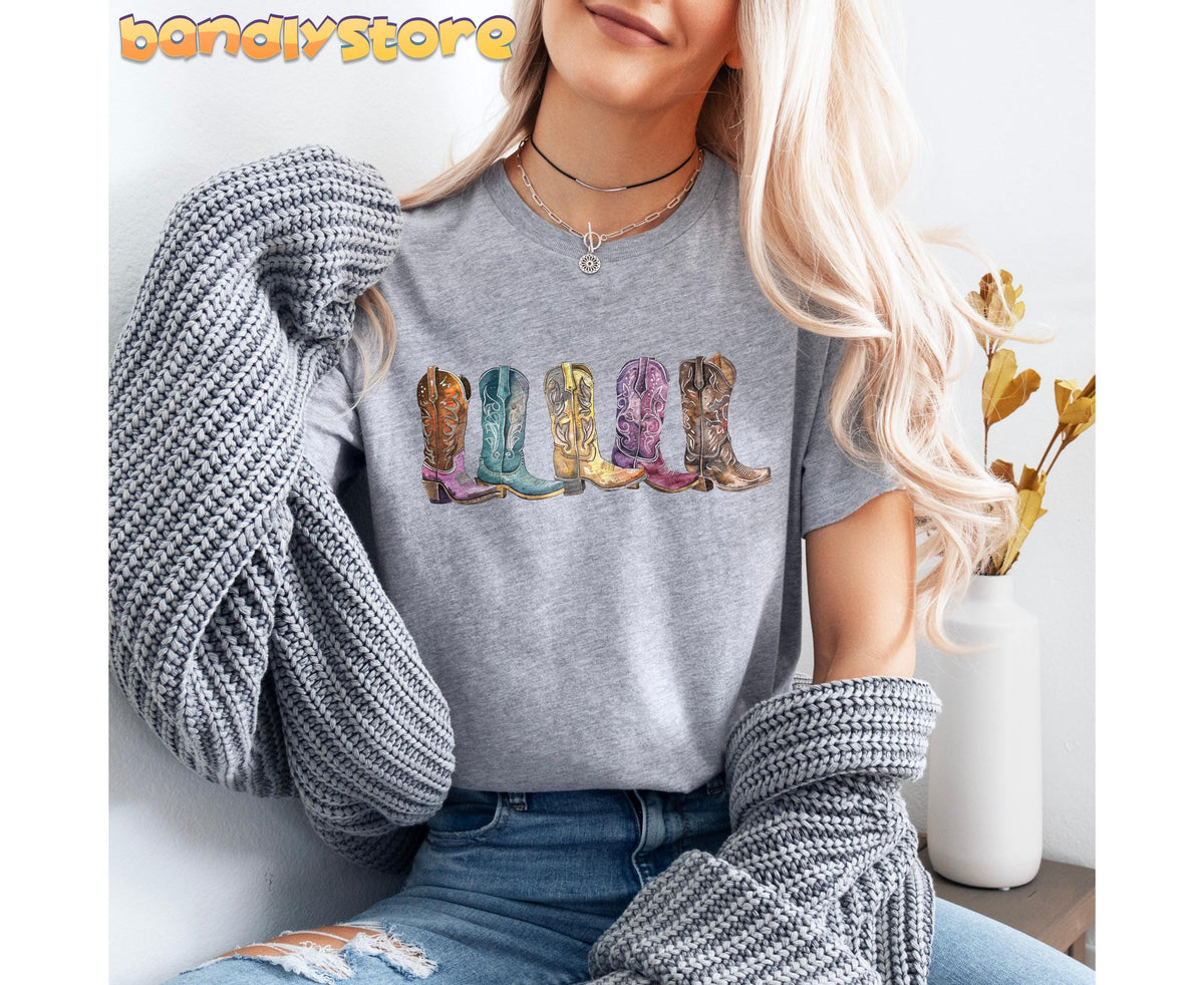 Cowgirl Boots T-Shirt in Athletic Heather on a woman holding a knit sweater beside a white vase.