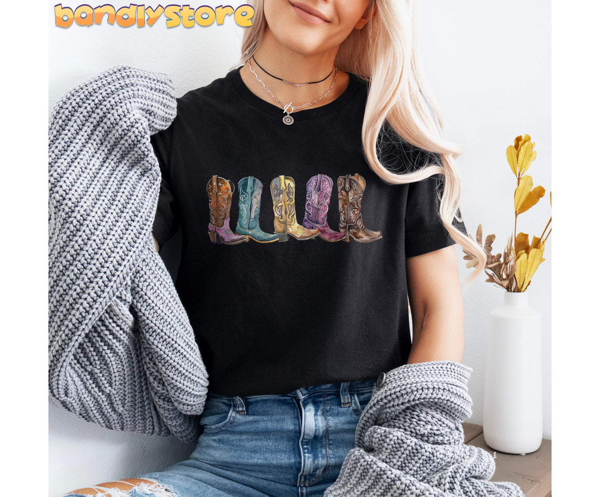 Cowgirl Boots T-Shirt in black front-view on a person holding grey knitwear beside a white vase.