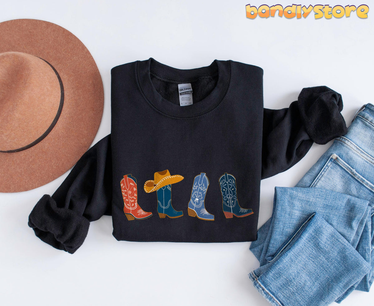 Cowgirl Boots Sweatshirt in black laid flat showing four boot designs beside a brown hat and blue jeans.