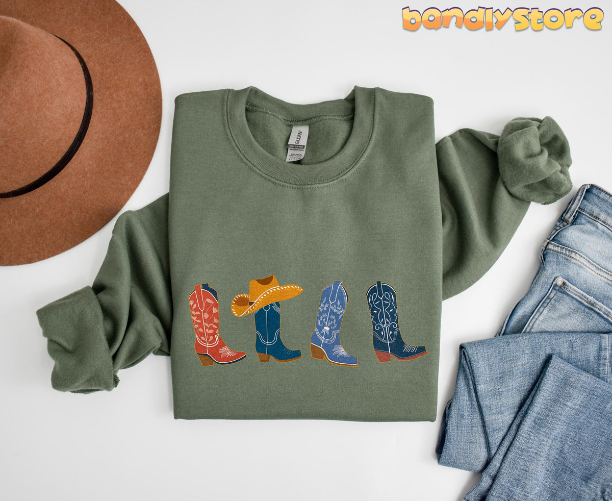 Cowgirl Boots Sweatshirt in military green laid flat from above beside a brown hat and blue jeans.