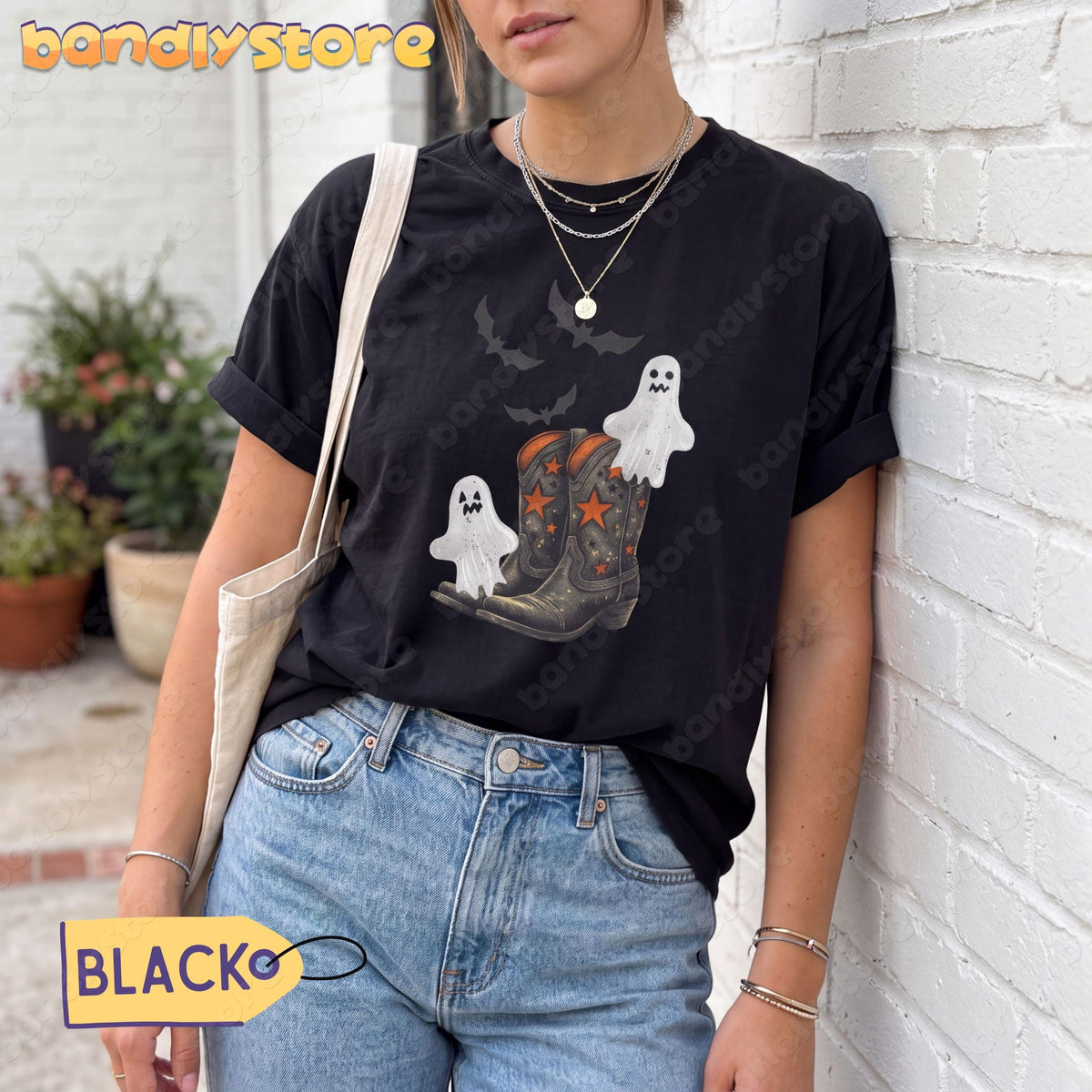 Vintage Cowgirl Boots and Ghosts T-Shirt in black on a person leaning against a white brick wall near potted plants.