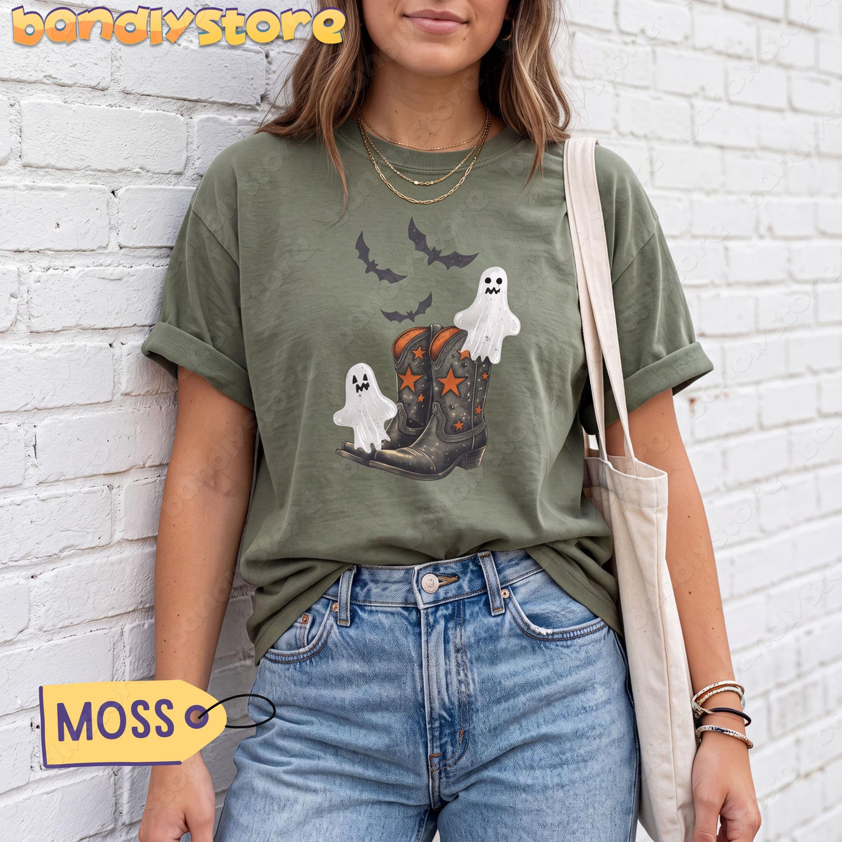 Vintage Cowgirl Boots and Ghosts T-Shirt in moss on a person against a white brick wall holding a tote bag.