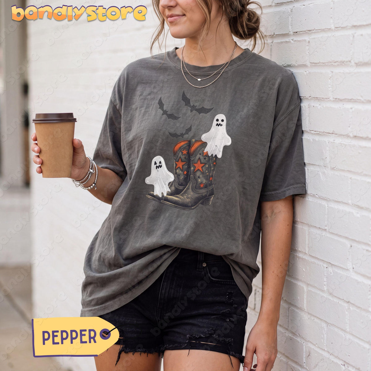 Vintage Cowgirl Boots and Ghosts T-Shirt in Pepper worn by a woman leaning against a white brick wall holding a coffee cup.