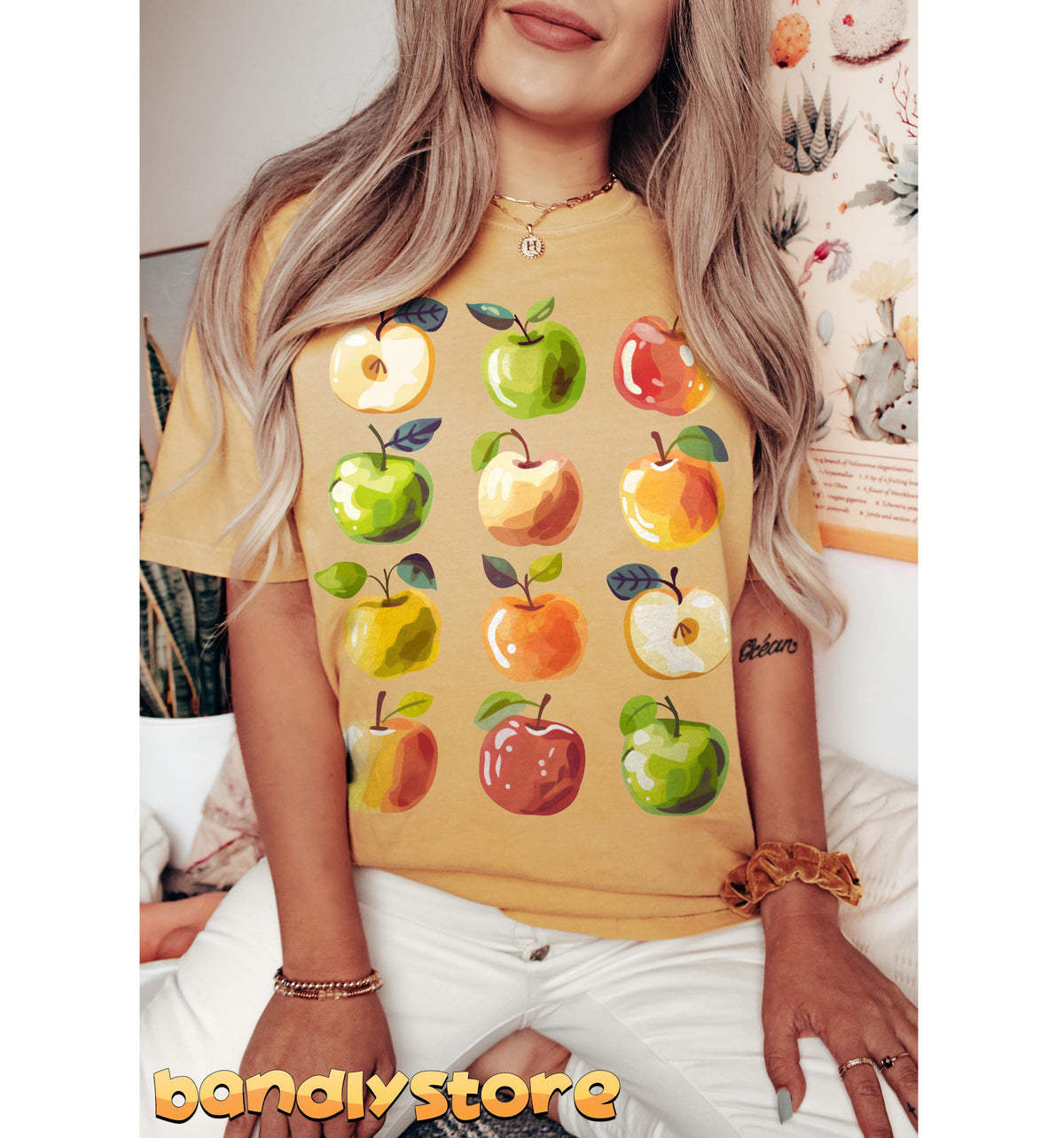 Cute Apples T-Shirt on a seated person facing forward beside a potted plant and botanical poster in Mustard
