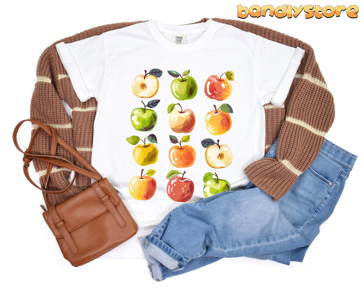 Cute Apples T-Shirt laid flat beside brown cardigan, blue jeans and brown bag in White