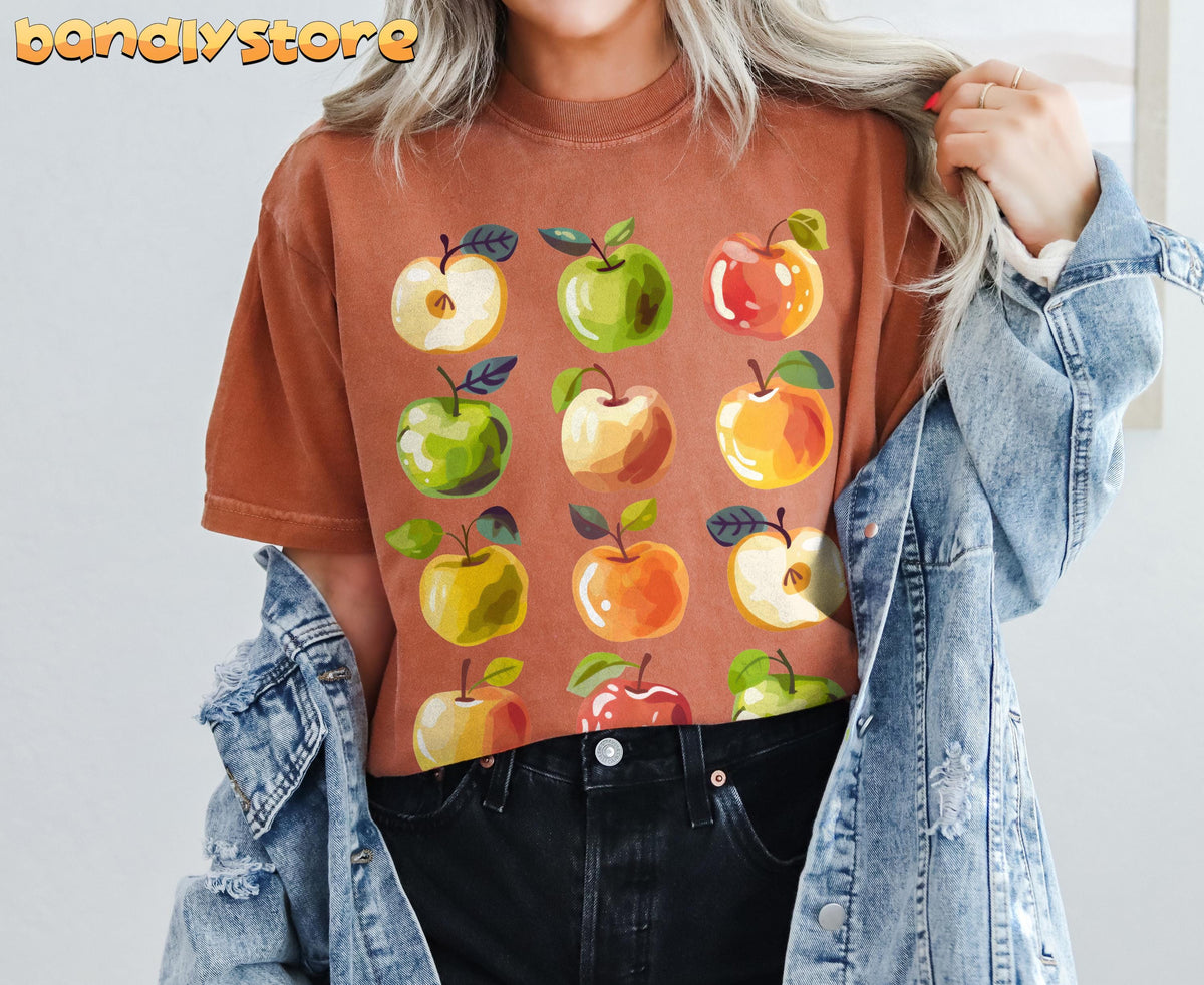 Cute Apples T-Shirt on a person facing forward, rust-brown tee with apple print, denim jacket and black jeans in Yam