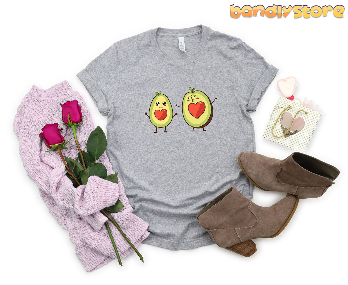 Cute Avocado Love T-Shirt in Athletic Heather flat-laid from above beside sweater, roses, boots and gift bag.