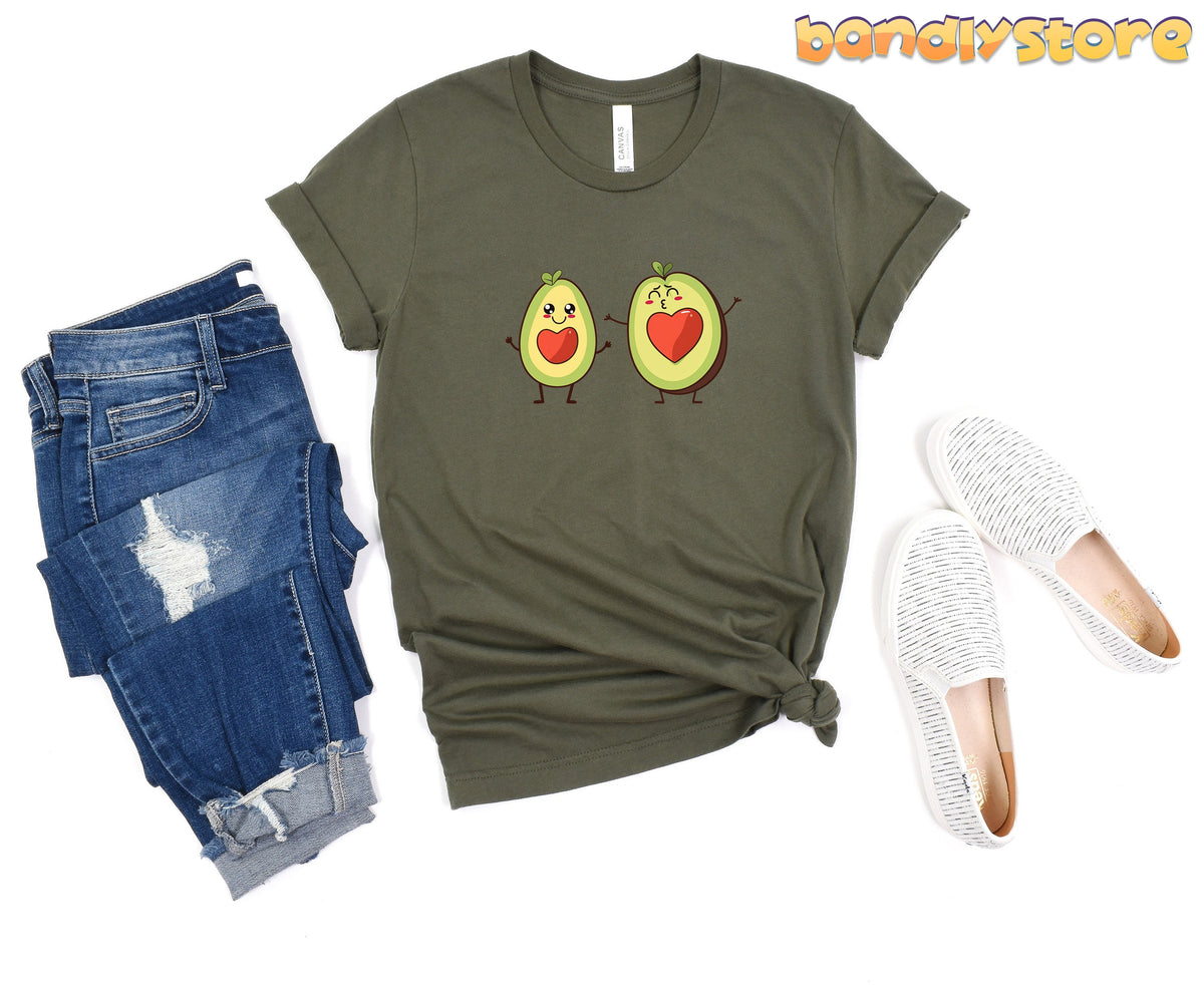 Cute Avocado Love T-Shirt in military green laid flat beside ripped jeans and white slip-on shoes.