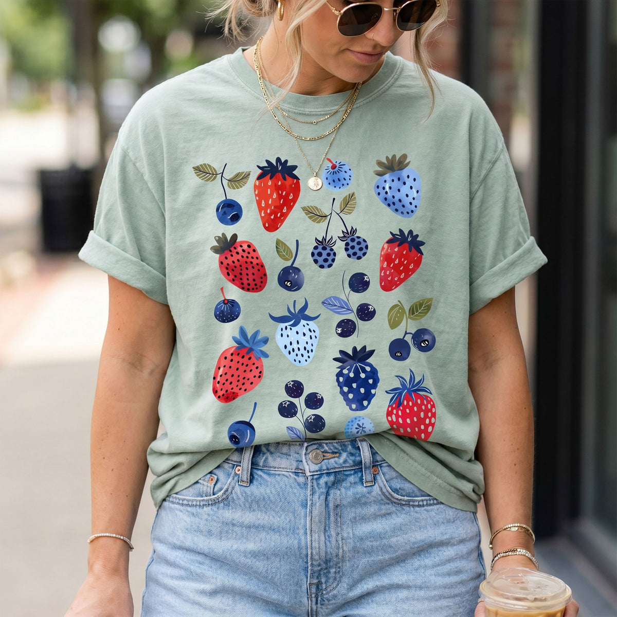 Cute Berry T-Shirt in Bay, worn front-view outdoors with rolled sleeves, jeans, layered gold necklaces and an iced drink.