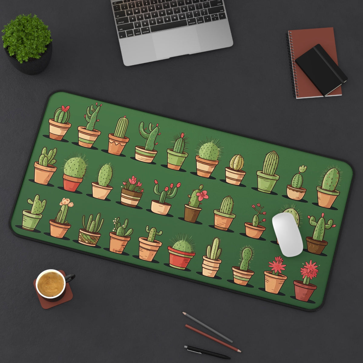 Cute Cacti Desk Mat 16 × 32 inches on a dark desk from above beside a laptop, plant, notebooks, coffee, pencils and mouse.