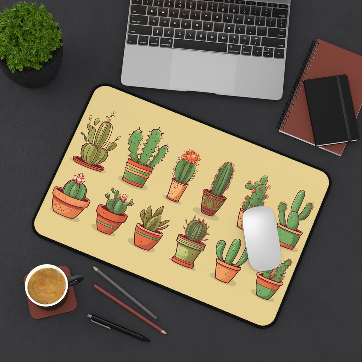Cute Cactuses Desk Mat from above on dark desk beside laptop, plant, notebooks, coffee, pens and mouse, 12 × 18 inches.