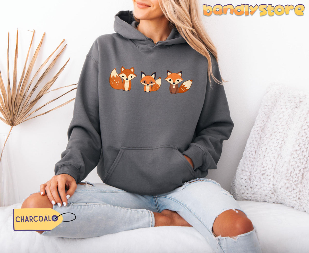 Cute Foxes Hoodie in charcoal, modelled front-on indoors beside a dried palm and white cushion.