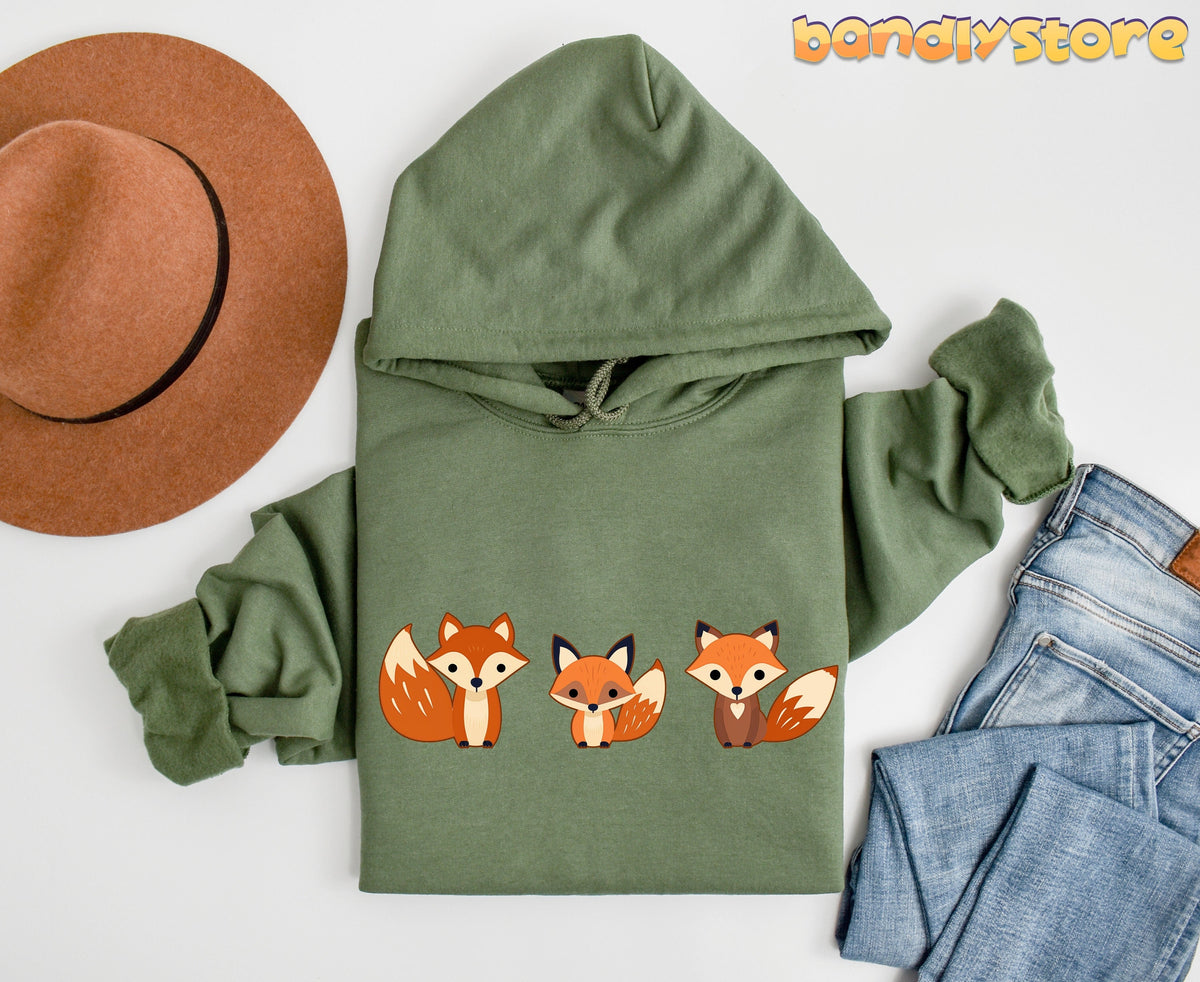 Cute Foxes Hoodie in forest green laid flat beside a brown hat and blue jeans.
