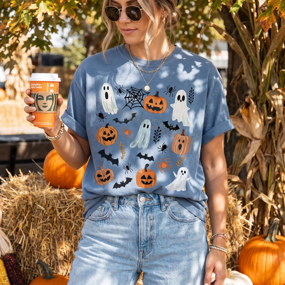 Cute Spooky Ghosts Pumpkins T-Shirt in Blue Jean on a woman holding a cup beside hay bales and pumpkins outdoors.
