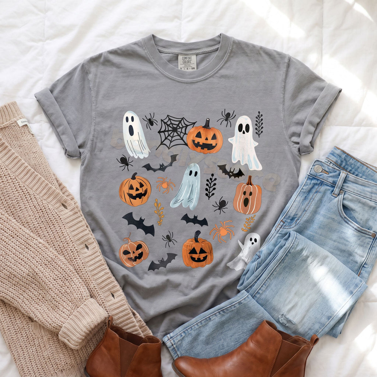 Cute Spooky Ghosts Pumpkins T-Shirt in grey laid flat on white bedding by a beige sweater, blue jeans and brown boots.