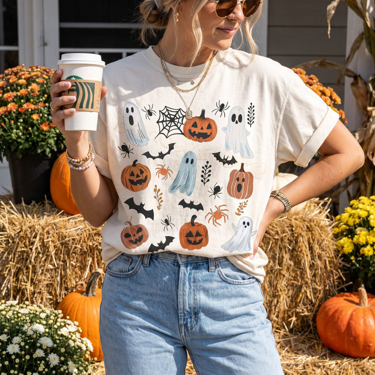 Cute Spooky Ghosts Pumpkins T-Shirt in ivory, worn outdoors among hay bales, pumpkins and fall flowers as the model holds a coffee cup.