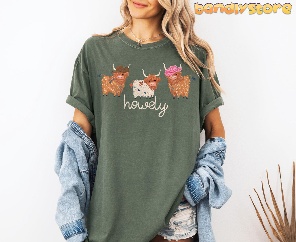 Cute Highland Cows T-Shirt in moss on a model facing forward against a white wall with a denim jacket.