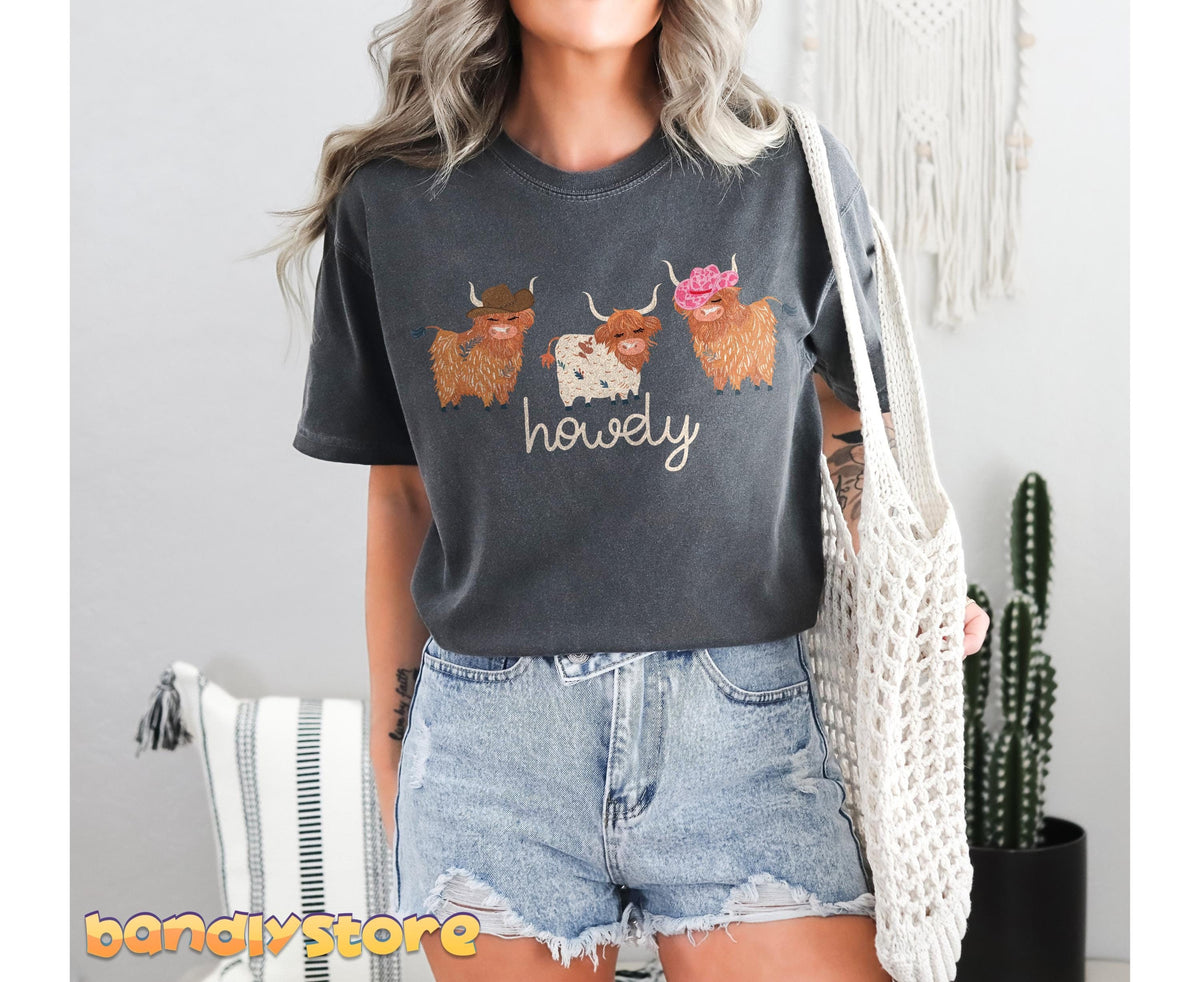 Cute Highland Cows T-Shirt in Pepper worn front-facing indoors beside cactus, macrame and striped pillow.