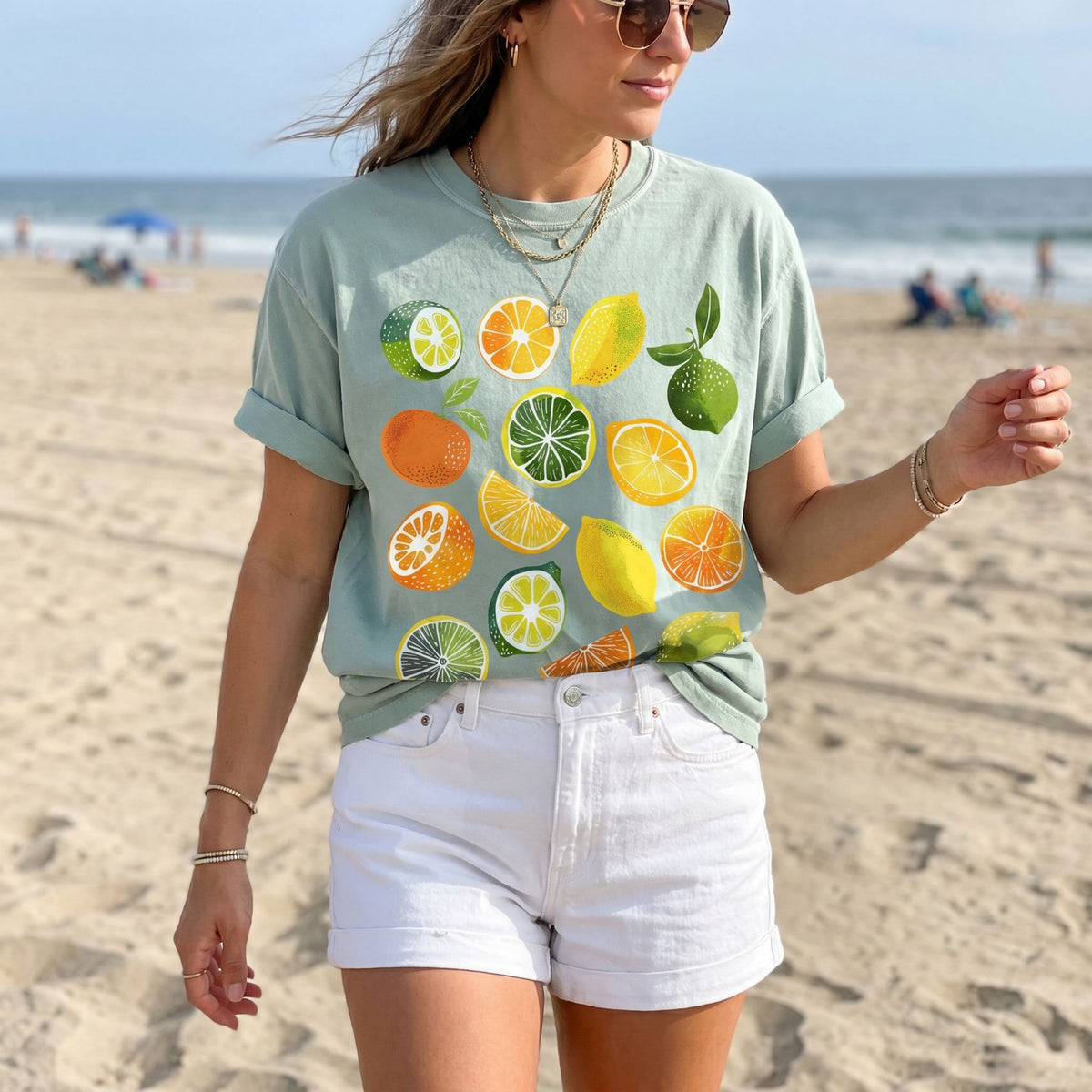 Cute Lemons And Oranges T-Shirt in bay worn by a woman standing on a sandy beach near the ocean.