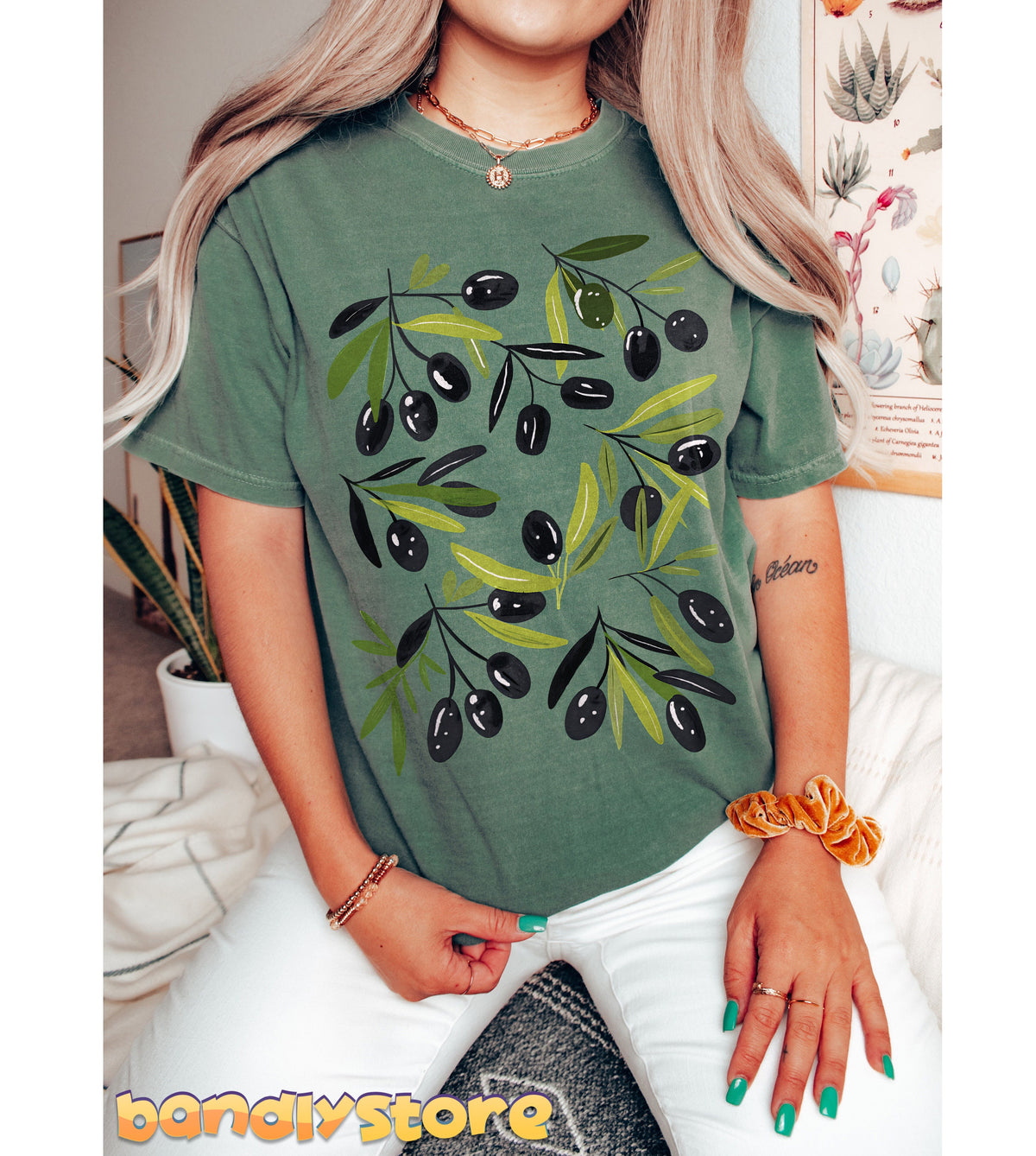 Cute Olives T-Shirt in moss on a seated person, front view indoors with plants and posters.