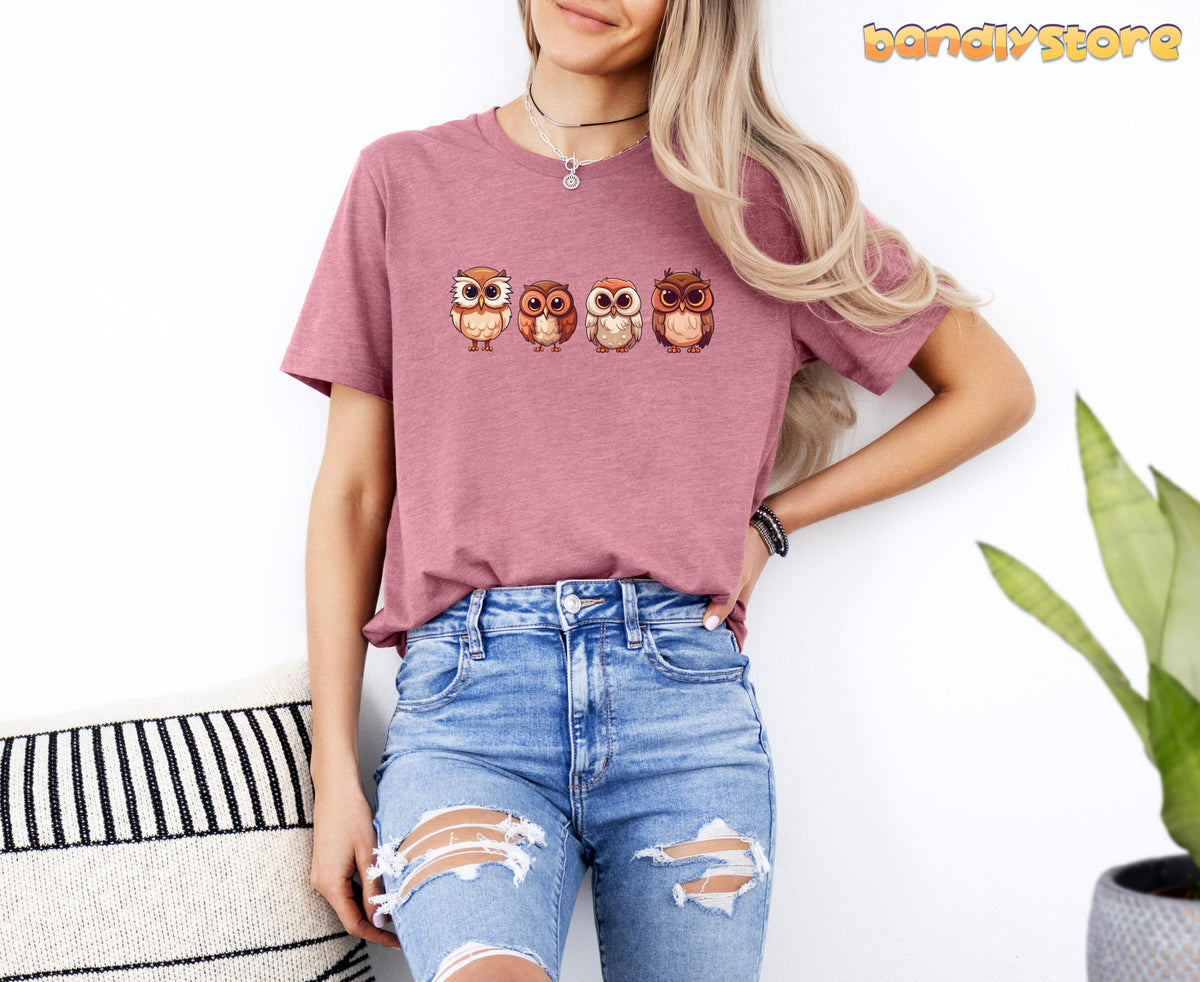 Cute Owl T-Shirt in Heather Mauve on a model standing against a white wall next to a striped pillow and potted plant.