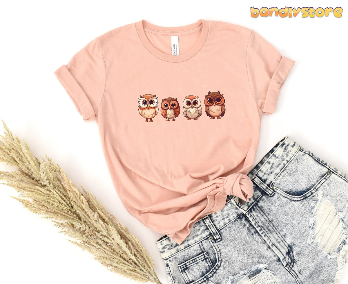 Cute Owl T-Shirt in heather peach flat-laid with rolled sleeves beside dried grass and ripped denim shorts.