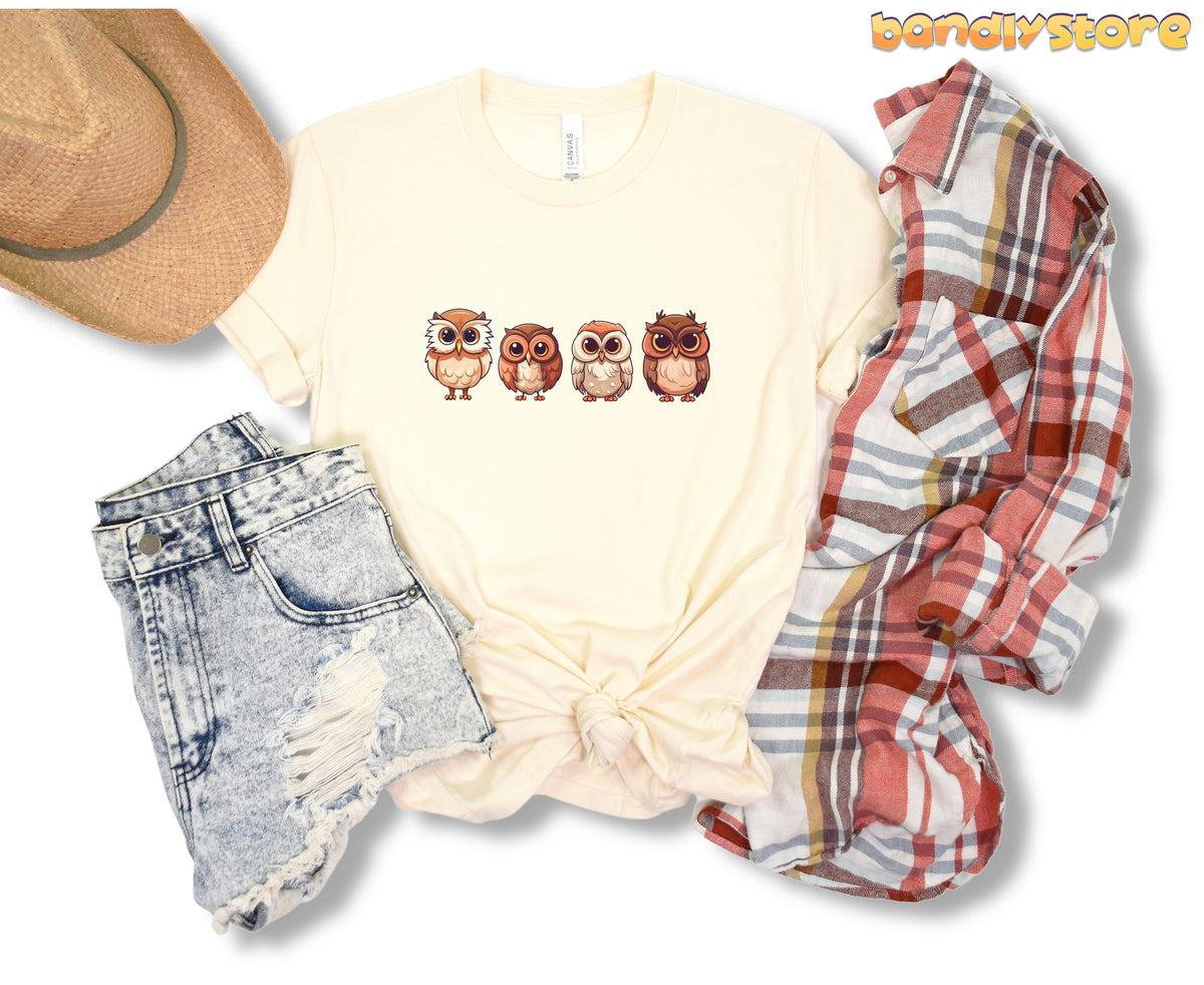 Cute Owl T-Shirt in natural laid flat beside a straw hat, denim shorts and plaid shirt.