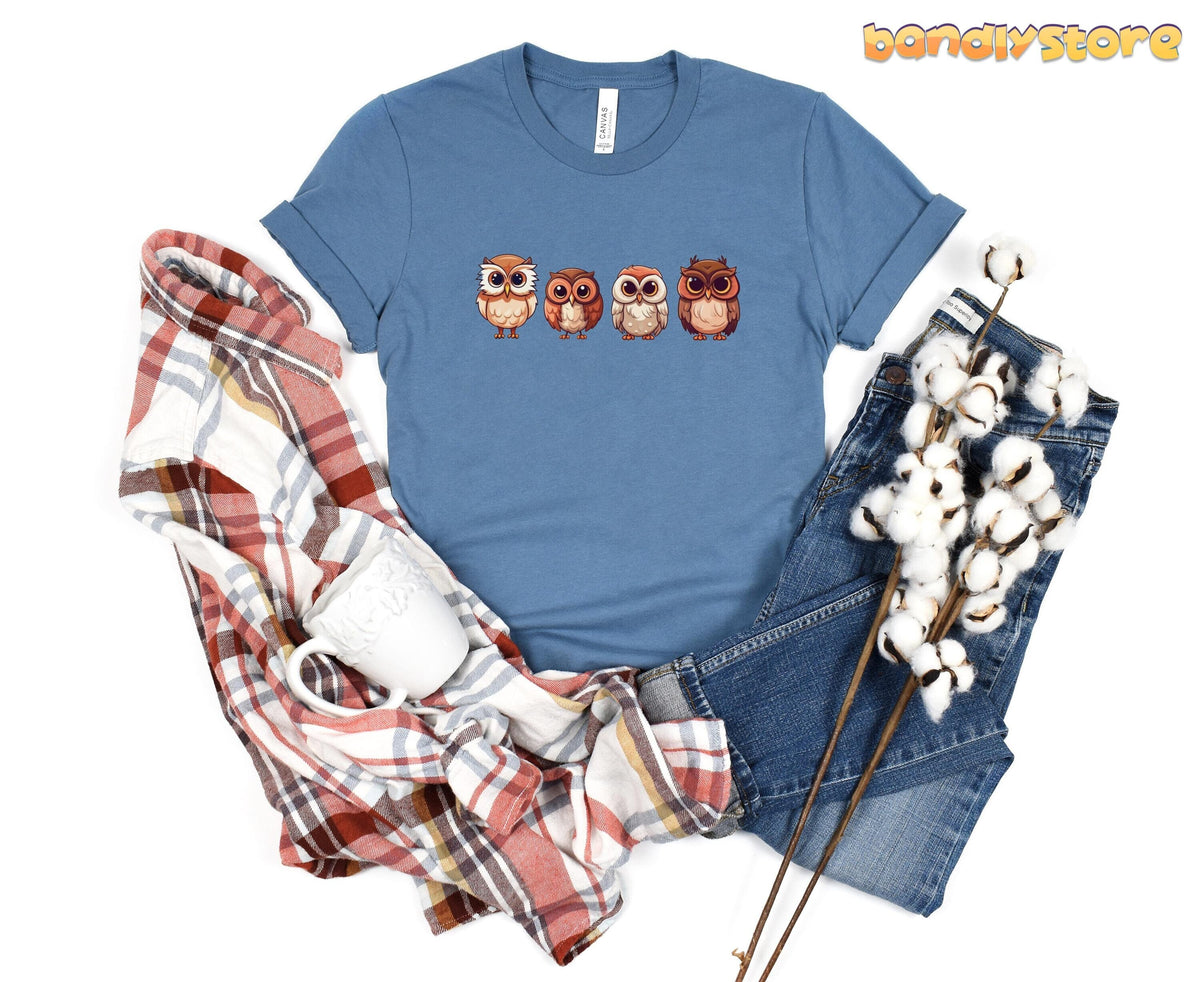 Cute Owl T-Shirt in steel blue flat-laid with plaid shirt, mug, jeans and cotton stems.