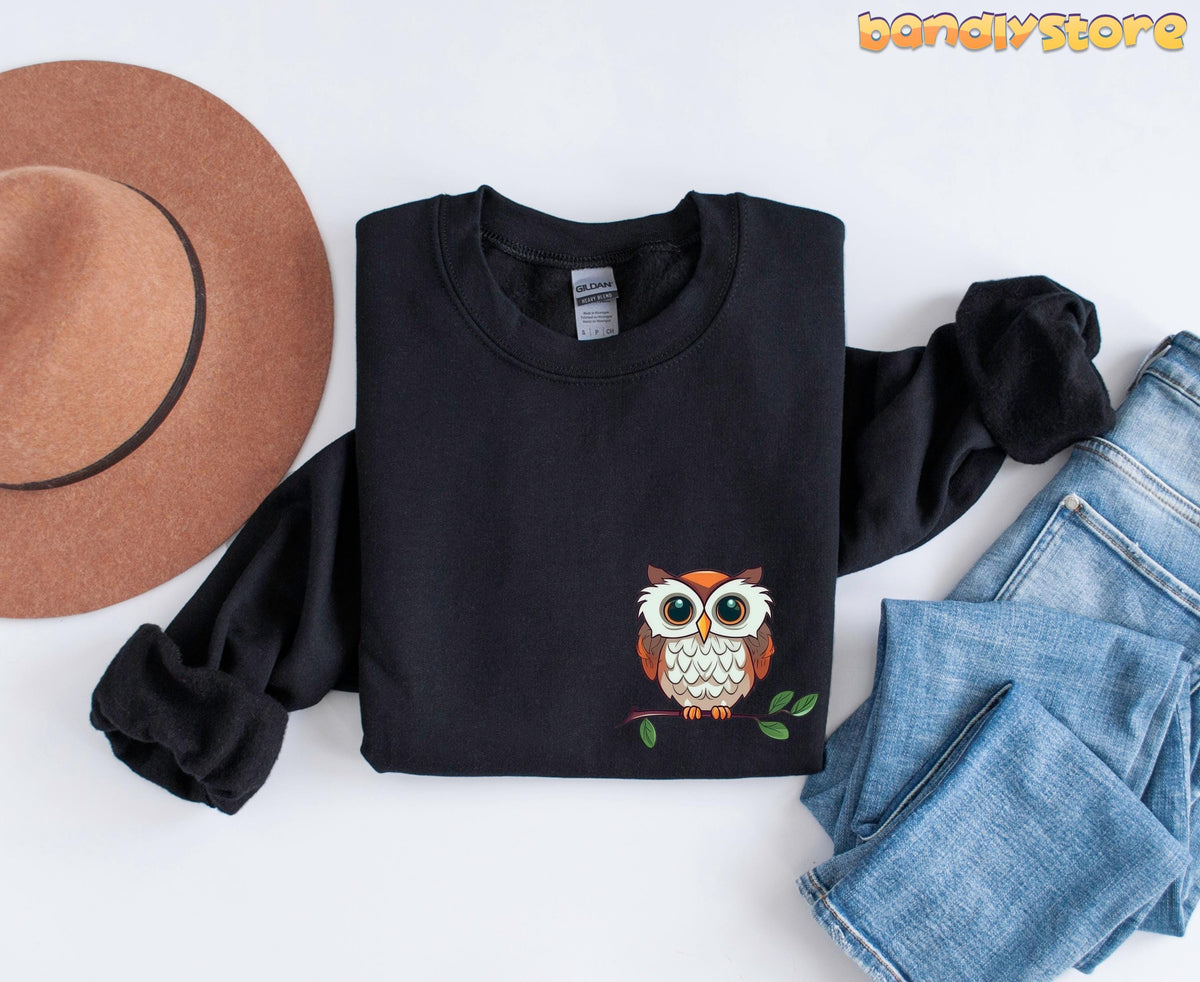 Cute Owl Sweatshirt with Pocket Design on black sweatshirt, flat lay with brown hat left and blue jeans right.