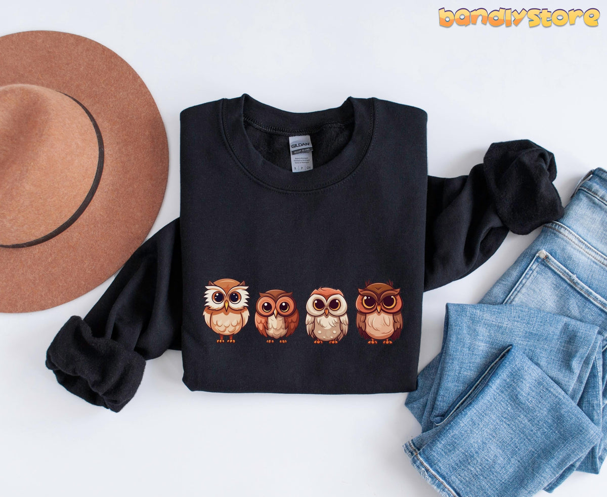 Cute Owl Sweatshirt black folded flat beside a hat and jeans on a white surface.