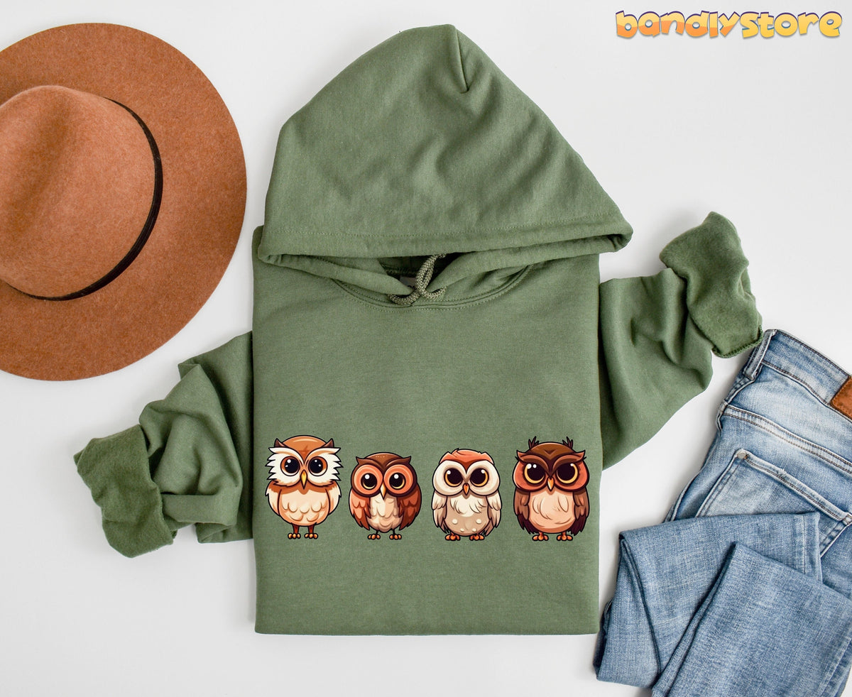 Cute Owl Hoodie in Military Green flat-laid from above beside a brown hat and blue jeans on white.