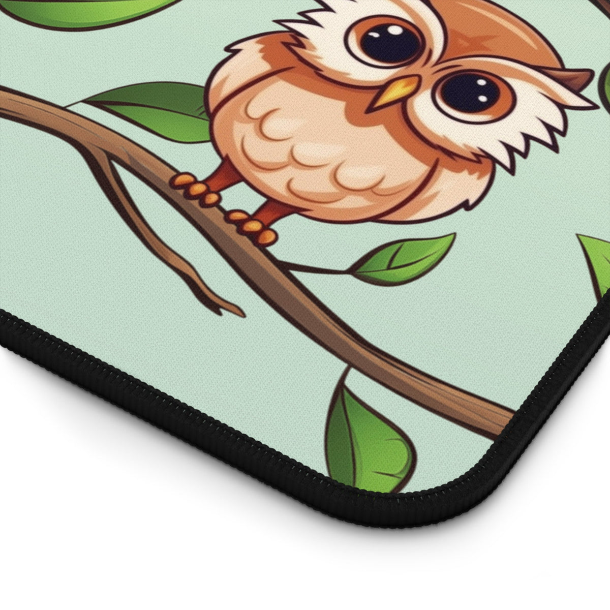 Cute Owls Desk Mat detail of black stitched corner with cartoon owl on branch among leaves.