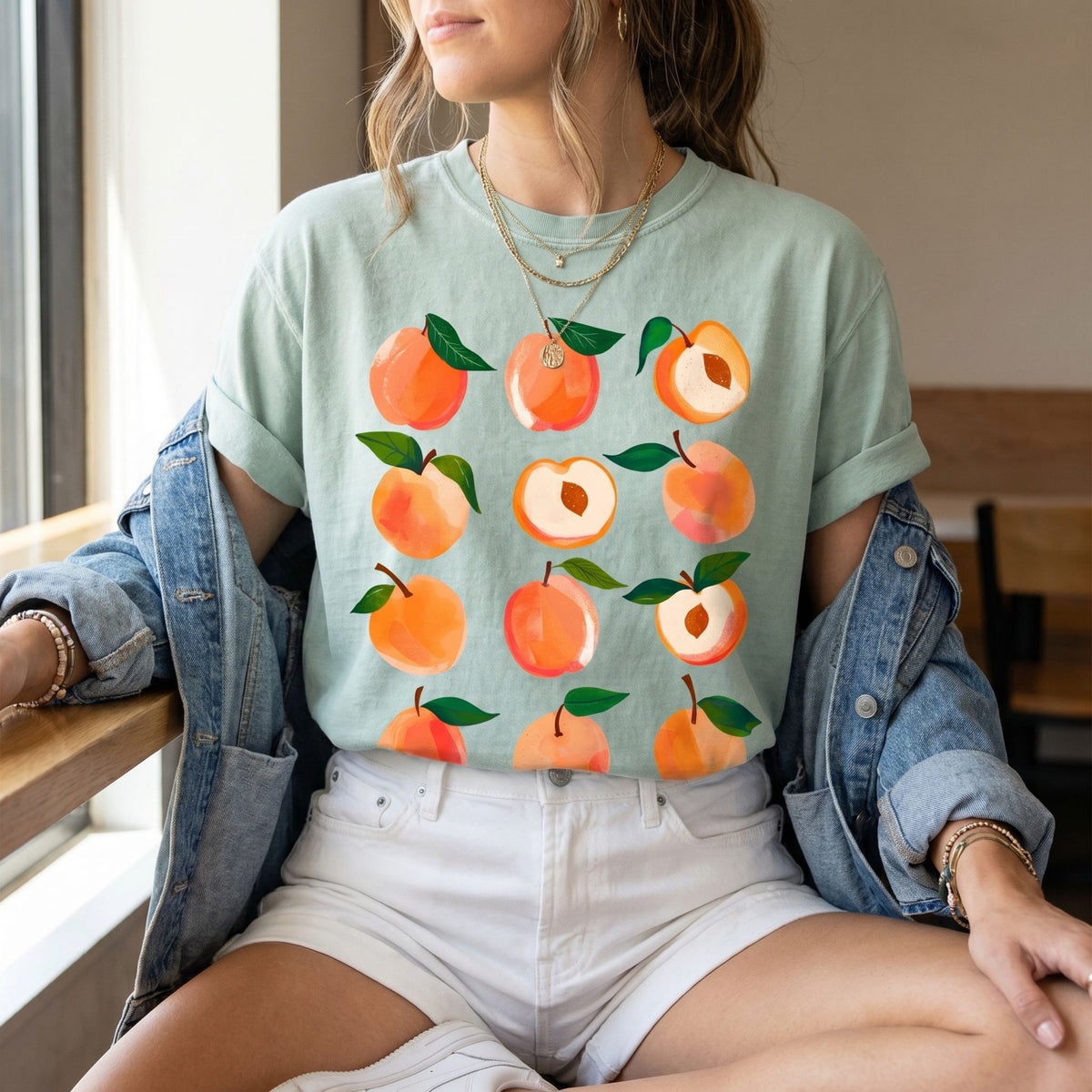 Cute Peaches T-Shirt in bay on model seated by window in open denim jacket and white shorts.