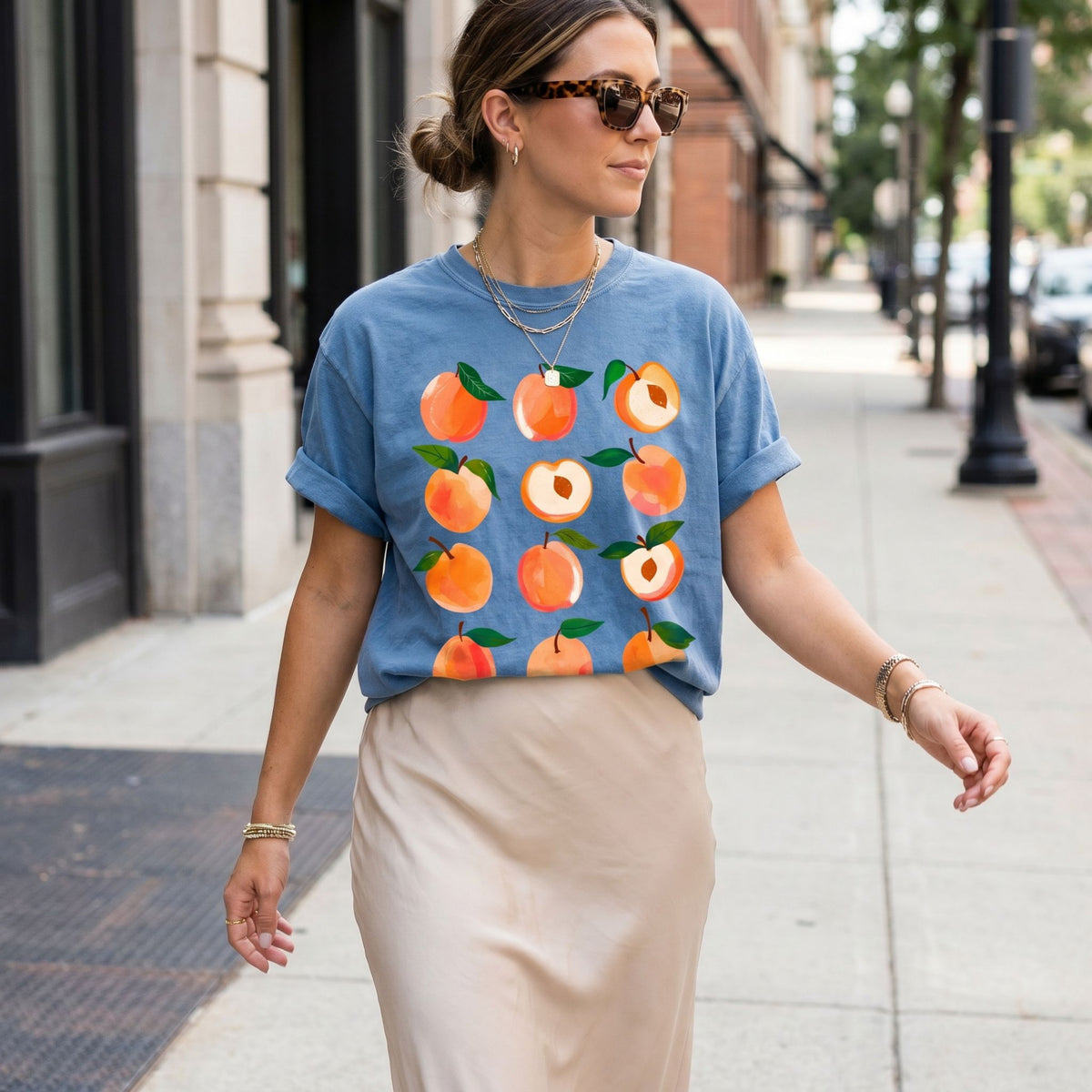 Cute Peaches T-Shirt in Blue Jean, worn on a city sidewalk with buildings and trees behind.