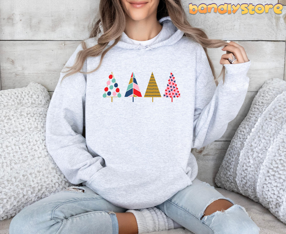 Cute Pine Trees Hoodie in Ash, worn front-facing by a seated person amid white pillows on a light wood wall.