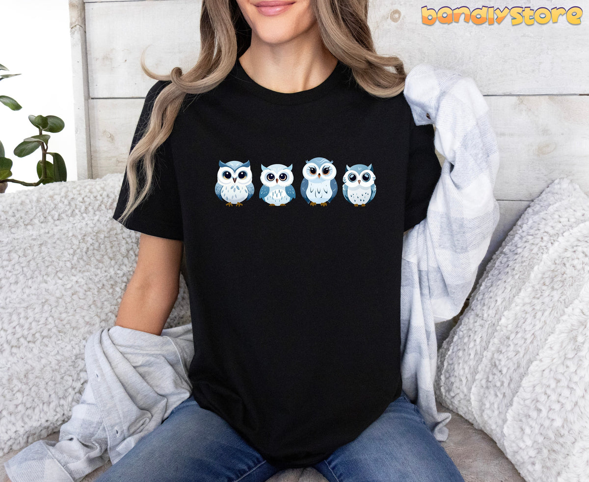 Cute Snow Owl T-Shirt on black tee, seated model front view with four blue-white owls, couch and plaid shirt.